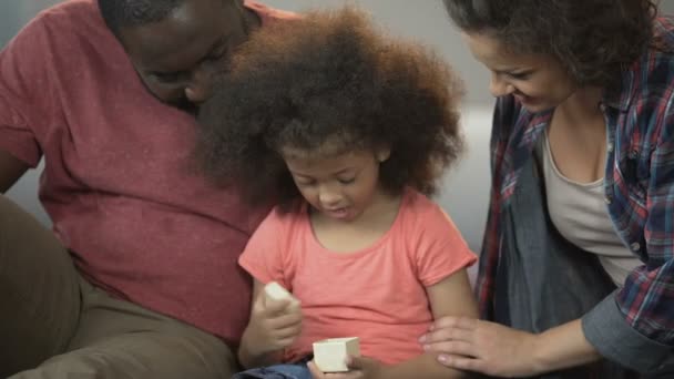 Радостная маленькая девочка открывает маленький подарок и благодарит любящих мать и отца — стоковое видео