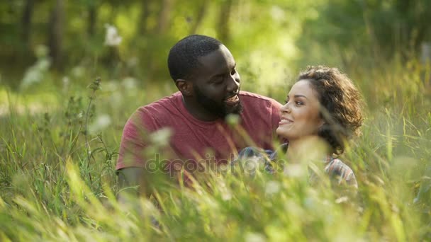 Pareja multirracial riendo y charlando mientras está acostado en la hierba, cita al aire libre — Vídeo de stock