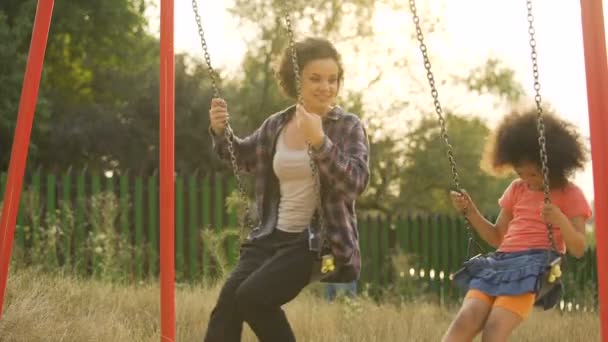 Two cheerful sisters moving back and forth on swings, outdoor child playground — Stock Video