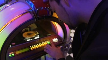 İyi şarkı bozuk para bırakarak ve tuşları bastırıyor eski müzik kutusu üzerinde seçmek çalışan adam