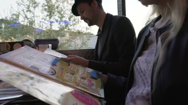 Couple assis sur la terrasse du café confortable et le menu de lecture, réunion avec des amis — Video