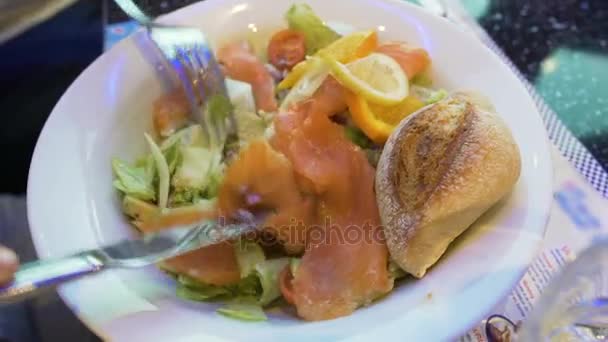 Mani che tengono posate affettare insalata con salmone, delizioso pranzo nel ristorante — Video Stock