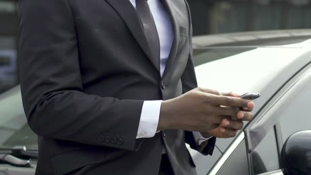 Αφρικανική αμερικανική άνθρωπος στον επαγγελματικό κοστούμι πληκτρολογώντας μήνυμα στέκεται κοντά στο αυτοκίνητό του — Αρχείο Βίντεο
