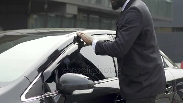 Чоловік у дорогому діловому костюмі протирає нову машину, задоволений покупкою автомобіля — стокове відео
