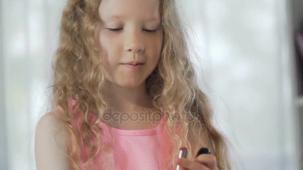 Pequeña niña de pie en el espejo delantero con lápiz labial rojo y aplicándolo, sonriendo — Vídeos de Stock