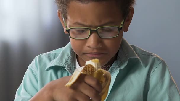 Criança pequena em óculos comendo banana, pausa para almoço na escola, dieta saudável — Vídeo de Stock