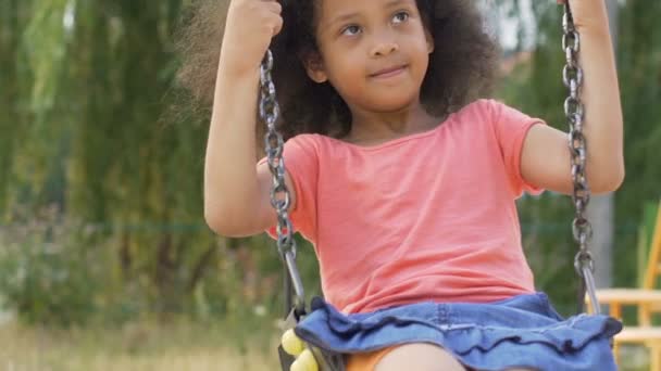 Kleines afrikanisch-amerikanisches Mädchen schaukelt im Sommer auf Spielplatz, Zeitlupe — Stockvideo