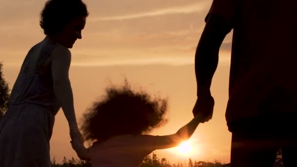 Silhuetas de pais se divertindo com sua filhinha contra o pôr do sol — Vídeo de Stock