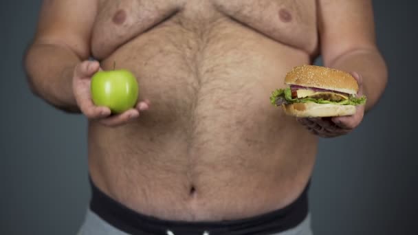 Hombre gordo elegir manzana en lugar de hamburguesa, mantener una dieta saludable, primer plano vientre — Vídeo de stock