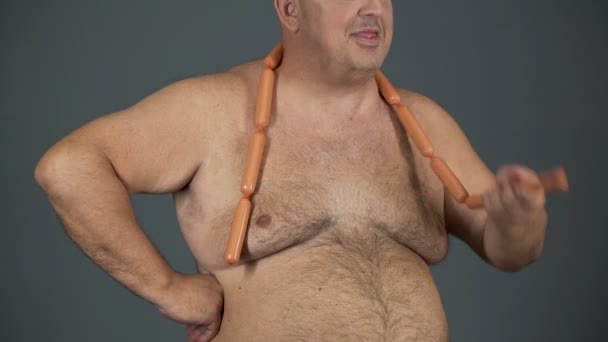 Пухкий чоловік їсть сосиски з апетитом, харчовою залежністю, ризиком діабету — стокове відео