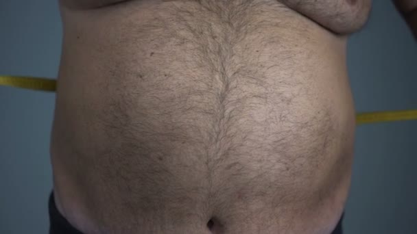 Депресивний товстий чоловік вимірює величезну животику, має проблеми зі здоров'ям, пасивний спосіб життя — стокове відео