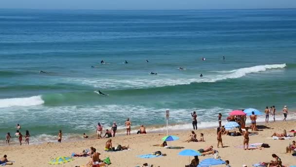 CASCAIS, PORTUGAL - CIRCA AUGUST 2014: People on the beach. Waves rolling onto beach with people sunbathing, surfers swimming in ocean, rest — Stock Video