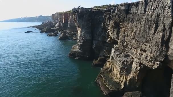 Ruhiges Meer und hohe felsige Klippen mit leichten Wellen, die gegen sie rollen, Höhle in den Klippen — Stockvideo