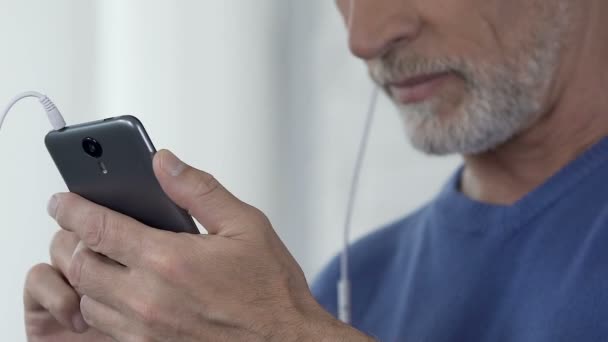 Мужчина составляет плейлист своих любимых песен на смартфоне, доступное приложение — стоковое видео