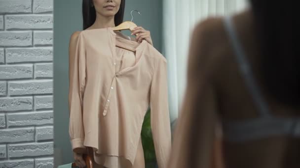 Hübsche Frau probiert Kleidung vor Spiegel im Zimmer, Vorbereitung für Date — Stockvideo