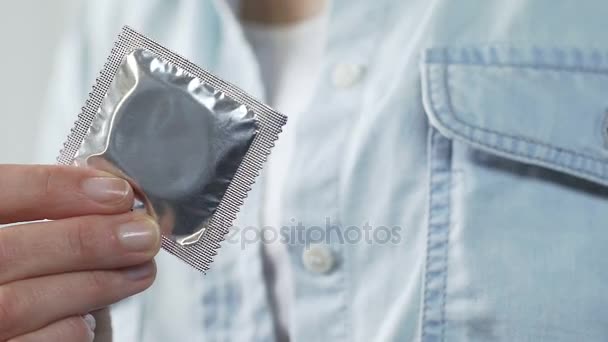 女孩手拿着密封的避孕套, 把它放入口袋的衬衫, 避孕 — 图库视频影像