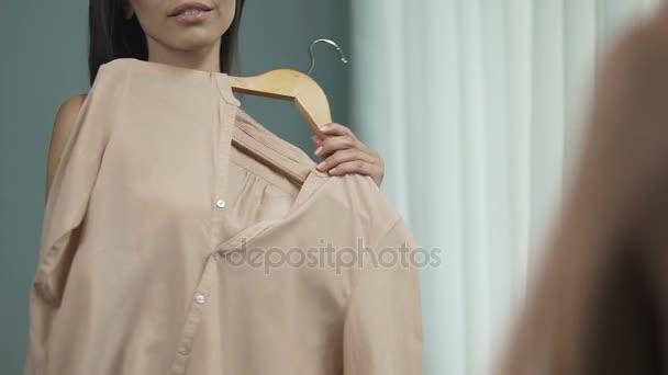 Привлекательная женщина стоит перед зеркалом, примеряет разные наряды, одежду — стоковое видео