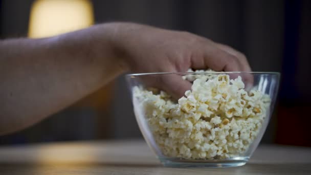 A férfi étkezési popcorn asztalon, egészségtelen ételek rabja tálból közelről — Stock videók
