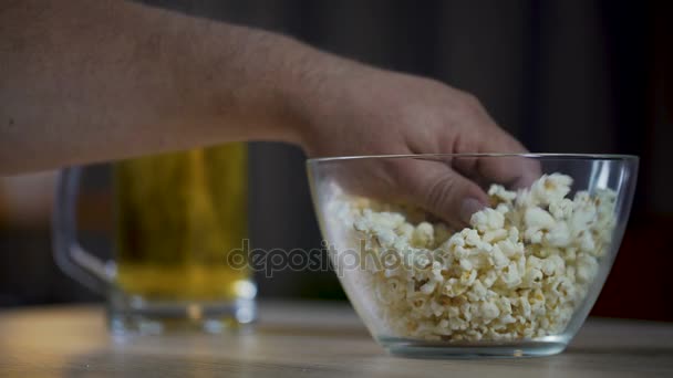 Hombre comiendo palomitas de maíz y bebiendo una cerveza mientras ve películas en casa, primer plano — Vídeo de stock