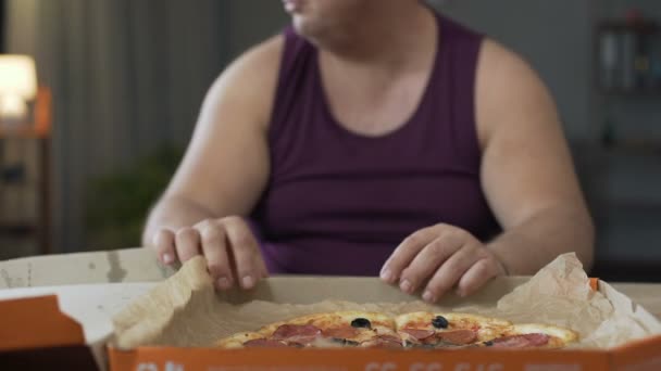 Hombre obeso mirando a su alrededor y devorando pizza grasosa por la noche, adicción a la comida chatarra — Vídeos de Stock