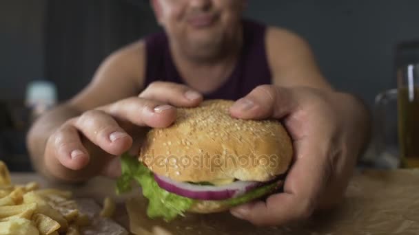 Fettleibige Mann nimmt großen Burger, aber nicht beißt es, Verweigerung von schlechten Essgewohnheiten — Stockvideo
