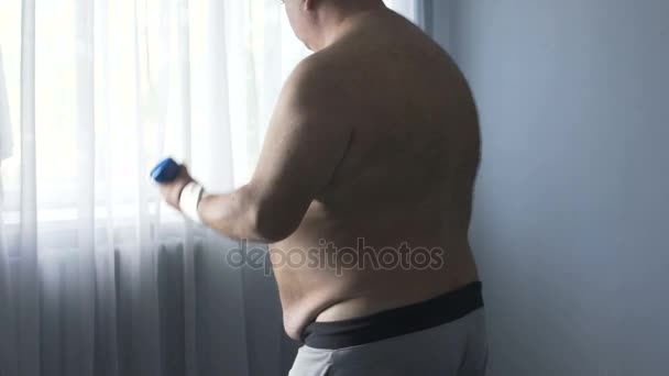 Hombre gordo haciendo deportes activamente, levantando pesas para perder peso, haciendo ejercicio en casa — Vídeos de Stock