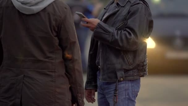 Двоє чоловіків в куртках замовляють таксі на відкритому повітрі, чекаючи водія таксі, щоб забрати їх — стокове відео