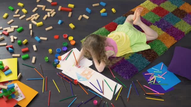 Niña bonita acostada en el suelo y dibujando con lápices de color sobre papel — Vídeos de Stock