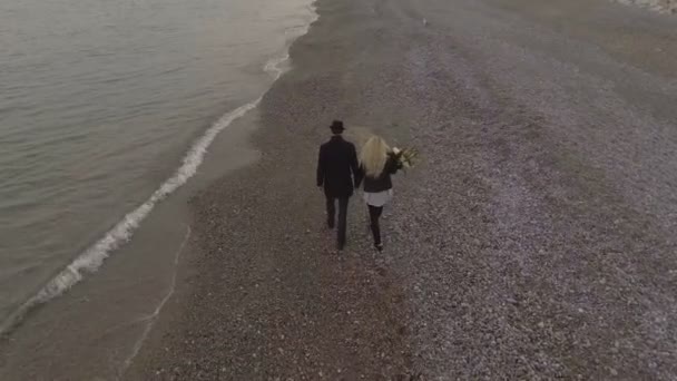 歩いて海岸持株の手で花を運ぶ女の子出会い系カップルの日付します。 — ストック動画