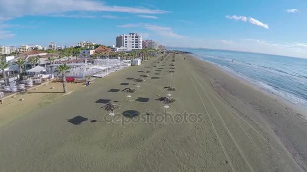 Беспилотник пролетает над соломенными зонтиками, стоящими на пляже в Ларнаке, Кипр — стоковое видео