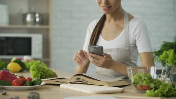 Ανάγνωση βιβλίου μαγειρικής και τον υπολογισμό των θερμίδων σε smartphone app η όμορφη γυναίκα — Αρχείο Βίντεο