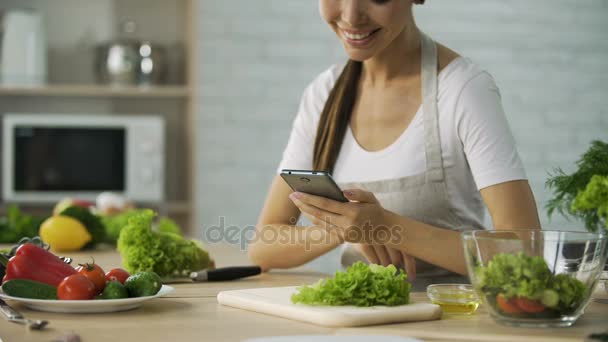 Lächelnde asiatische Mädchen, die Video-Rezept auf dem Smartphone vor dem Kochen Abendessen — Stockvideo