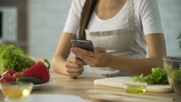 Woman choosing salad recipe on smartphone at the kitchen, cooking application — Stock Video