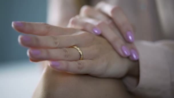 Крупный план женских рук, лежащих на коленях и касающихся золотого обручального кольца — стоковое видео