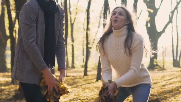 Pareja de adultos jóvenes genuinamente regocijarse y lanzar hojas de colores en el aire — Vídeo de stock