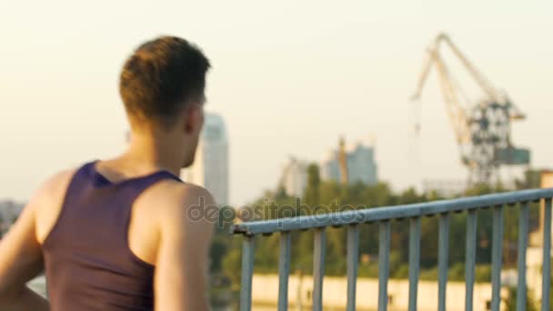 Athletic man jogging along bridge in big city, healthy way of life, slow-motion — Stock Video