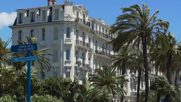 NICE, FRANCIA - CIRCA JUNIO 2016: Tráfico en la ciudad. Muchos coches que pasan por la construcción en Niza en el día soleado, palmeras balanceándose en el viento — Vídeos de Stock