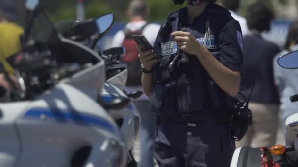 Female police officer standing next to motorbike, checking mobile phone on duty — Stock Video