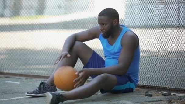 Nervöser Mann in Sportbekleidung, der allein in Stadionnähe sitzt und Ball hält, Verlierer — Stockvideo