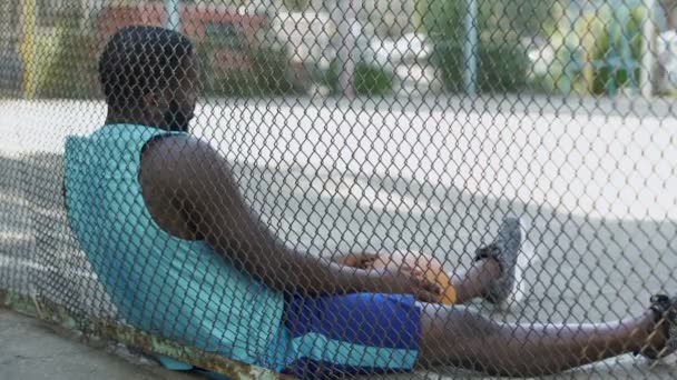 Одинокий недовольный мужчина сидит на баскетбольной площадке и держит мяч, депрессия — стоковое видео
