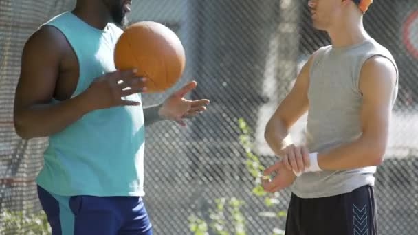 Dois amigos multirraciais atléticos discutindo o último jogo de basquete no estádio — Vídeo de Stock