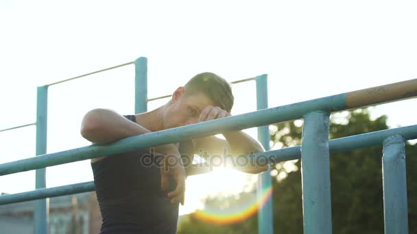 Pohledný mladý muž relaxační po tréninku na příčníky na západ slunce, sport, hobby — Stock video