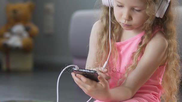 Engraçado feminino criança ouvindo música no fone de ouvido, segurando smartphone, close-up — Vídeo de Stock