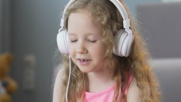 Niza chica de pelo rizado escuchando música en los auriculares y cantando canciones — Vídeos de Stock