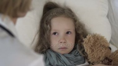 Kadın doktor sağlık evde, yatakta yatan hasta ağlayan kız ile konuşurken