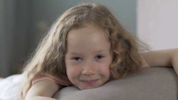 Alegre chica de pelo rizado acostado en el sofá y sonriendo a la cámara, la felicidad — Vídeos de Stock