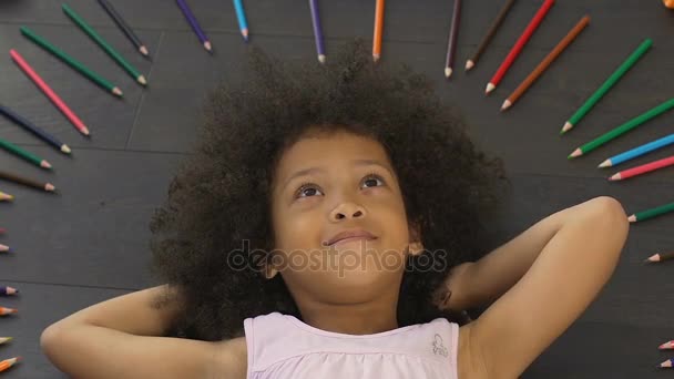 Niño pequeño con afro grande tumbado en el suelo y pensando en una nueva idea, imaginación — Vídeos de Stock
