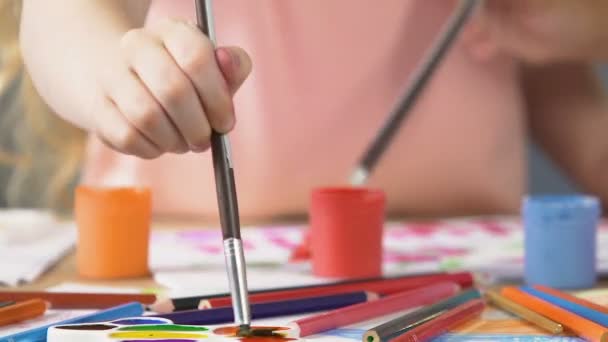Крупним планом маленька рука кладе пензлик для малювання в барвисту палітру, малюнок — стокове відео