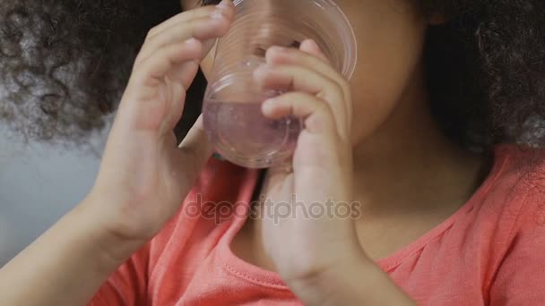 Маленька афро-американська дівчинка п'є чисту воду з пластикового скла, напої — стокове відео
