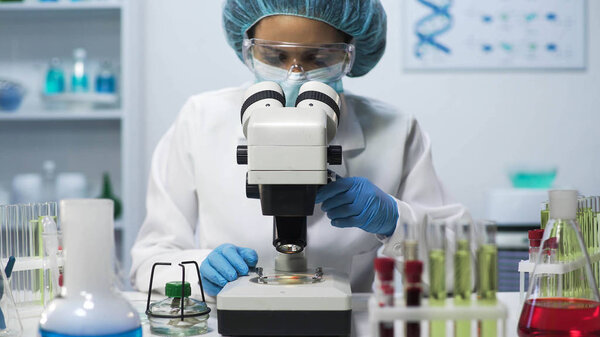 Female laboratory technician looking into microscope, doing biomedical research